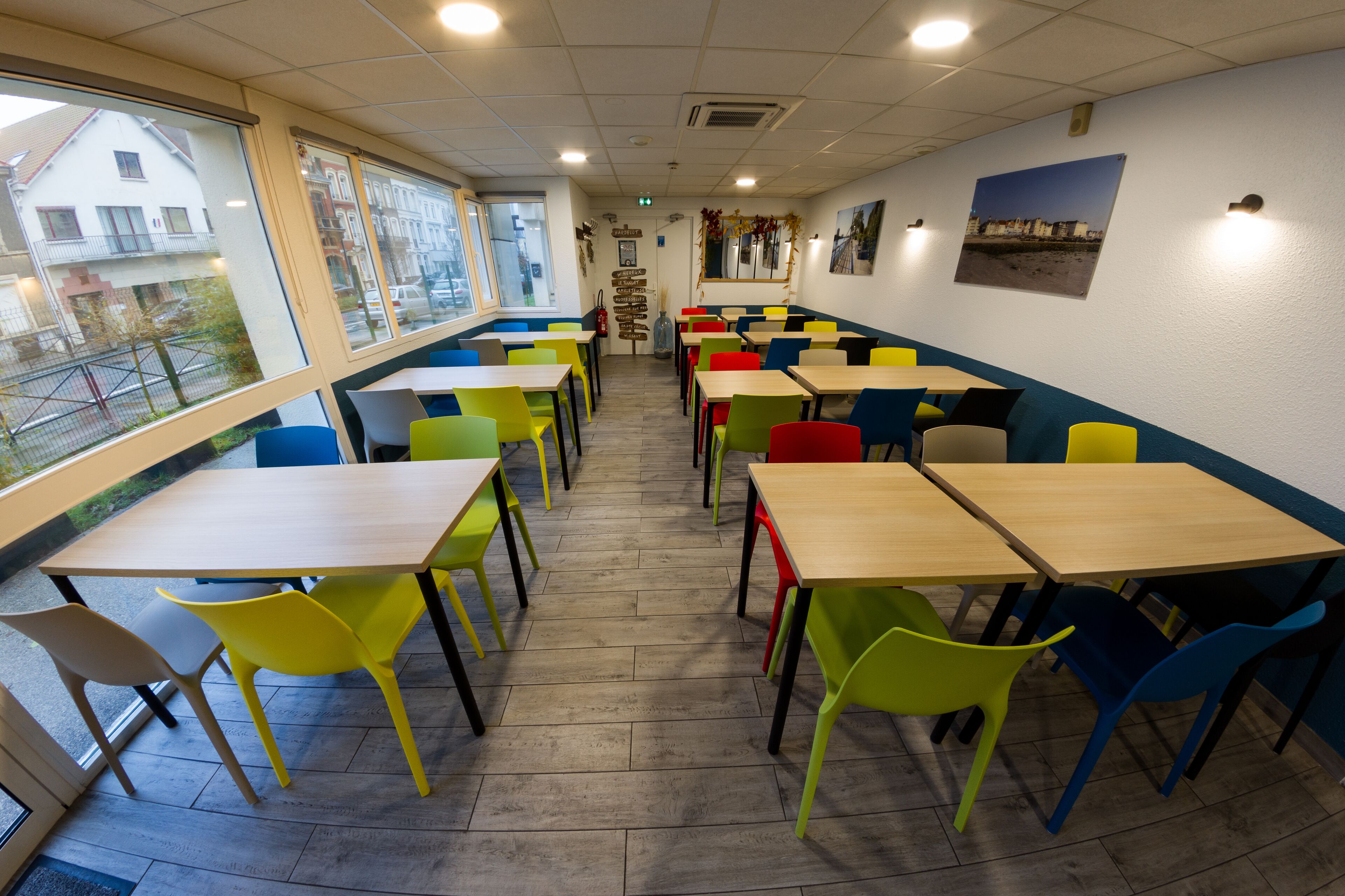 Un restaurant doté de nombreuses tables et chaises, de grandes fenêtres et offrant une vue sur les bâtiments environnants.