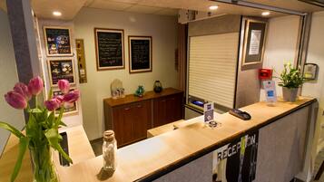 A hotel reception area with a wooden counter, a vase of pink tulips, and a framed menu on the wall.