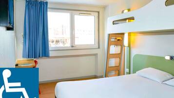 Habitación de hotel con cama, ventana con cortinas, mesita de noche y señal de accesibilidad para sillas de ruedas.