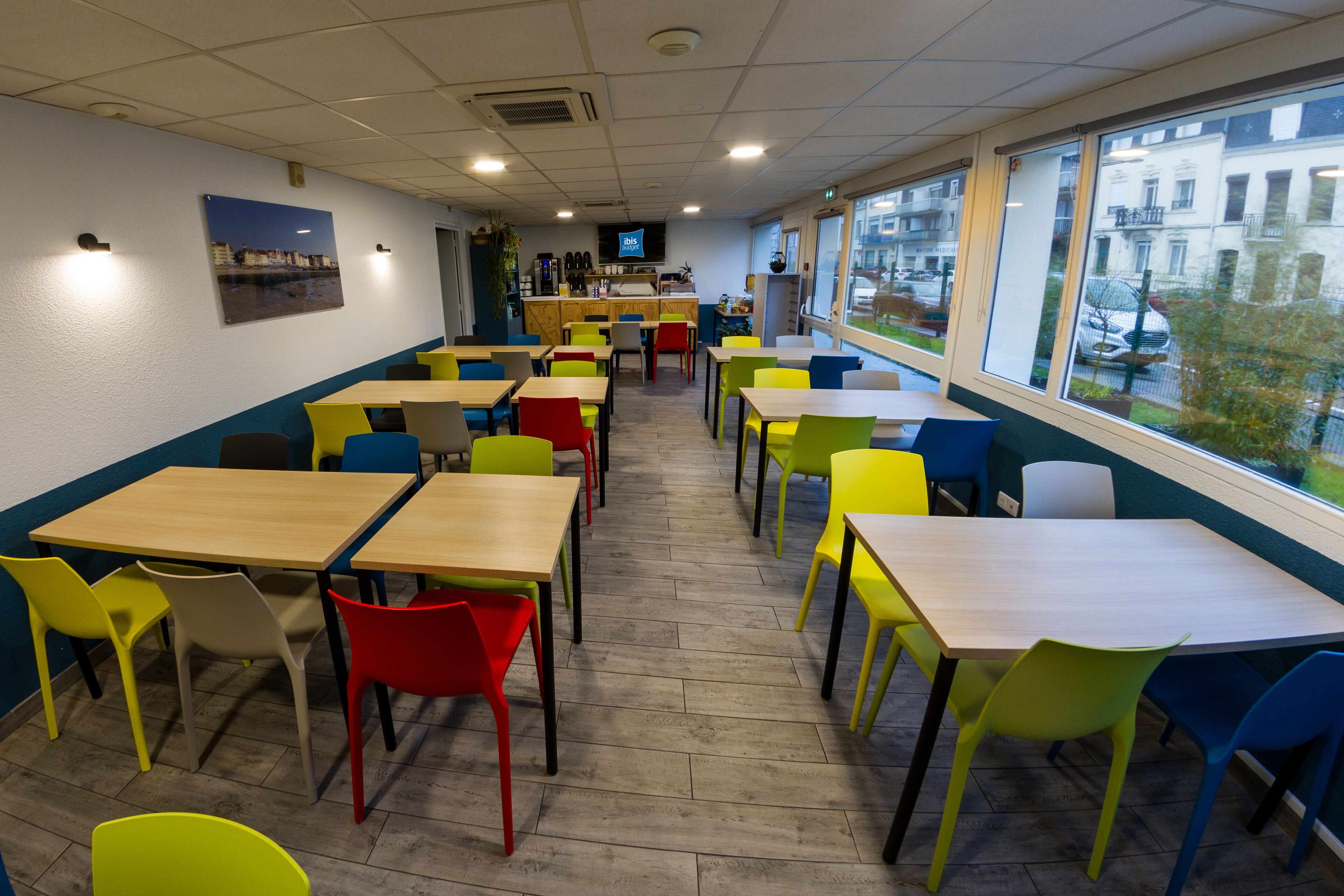 Un espace intérieur lumineux, doté de nombreuses tables et chaises, d’un écran de télévision et de grandes fenêtres donnant sur l’extérieur.