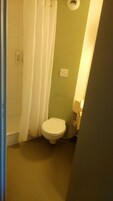 Un baño pequeño con inodoro, cortina de ducha y un accesorio de luz en la pared.