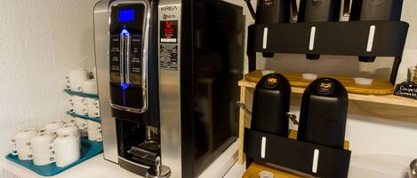 A coffee machine with a digital display, a coffee pod holder, and a tray of disposable cups.