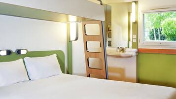 Ein Hotelzimmer mit Bett, Badezimmer mit Waschbecken und Spiegel sowie ein Fenster mit Blick auf Grünflächen.