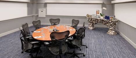 A conference room with a round table, eight chairs, a projector screen, and a decorative table centerpiece.
