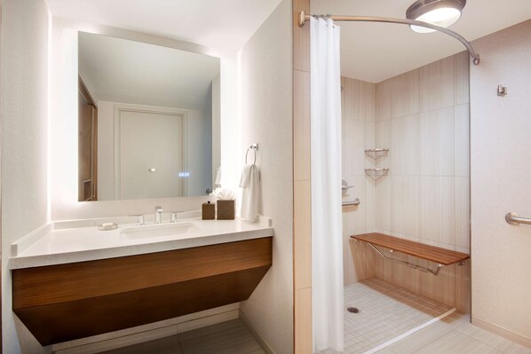 Un baño moderno con un espejo grande, un tocador de madera, una ducha con asiento y un perchero para toallas.