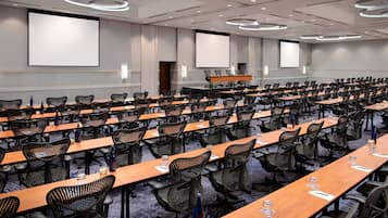 Une salle de conférence dotée de plusieurs tables et chaises, ainsi que de projecteurs et d’écrans.