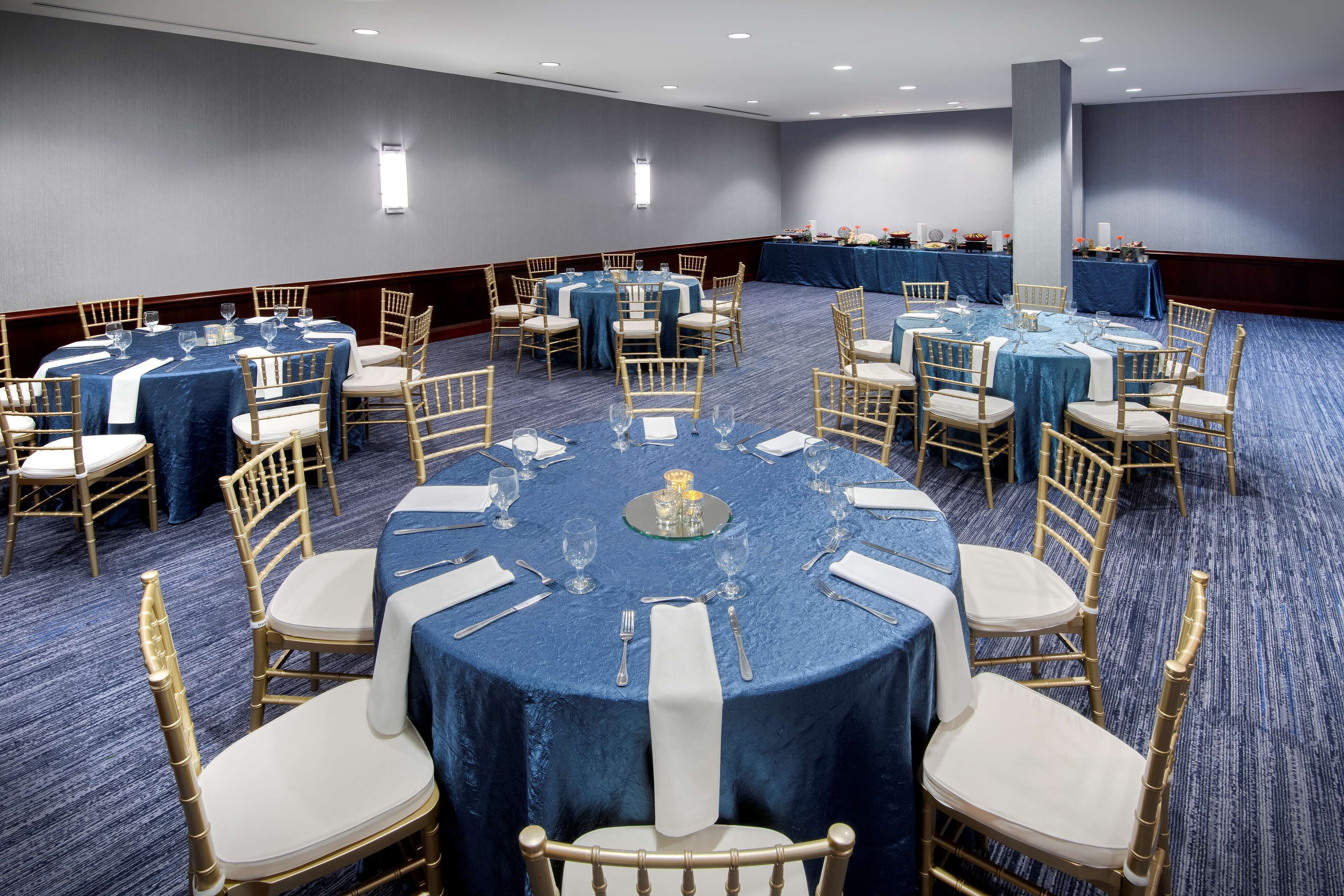 Une salle de conférence dotée de tables rondes, chacune entourée de chaises, et dont le sol est recouvert d’une moquette.