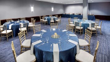 Une salle de conférence dotée de tables rondes, chacune entourée de chaises, et dont le sol est recouvert d’une moquette.