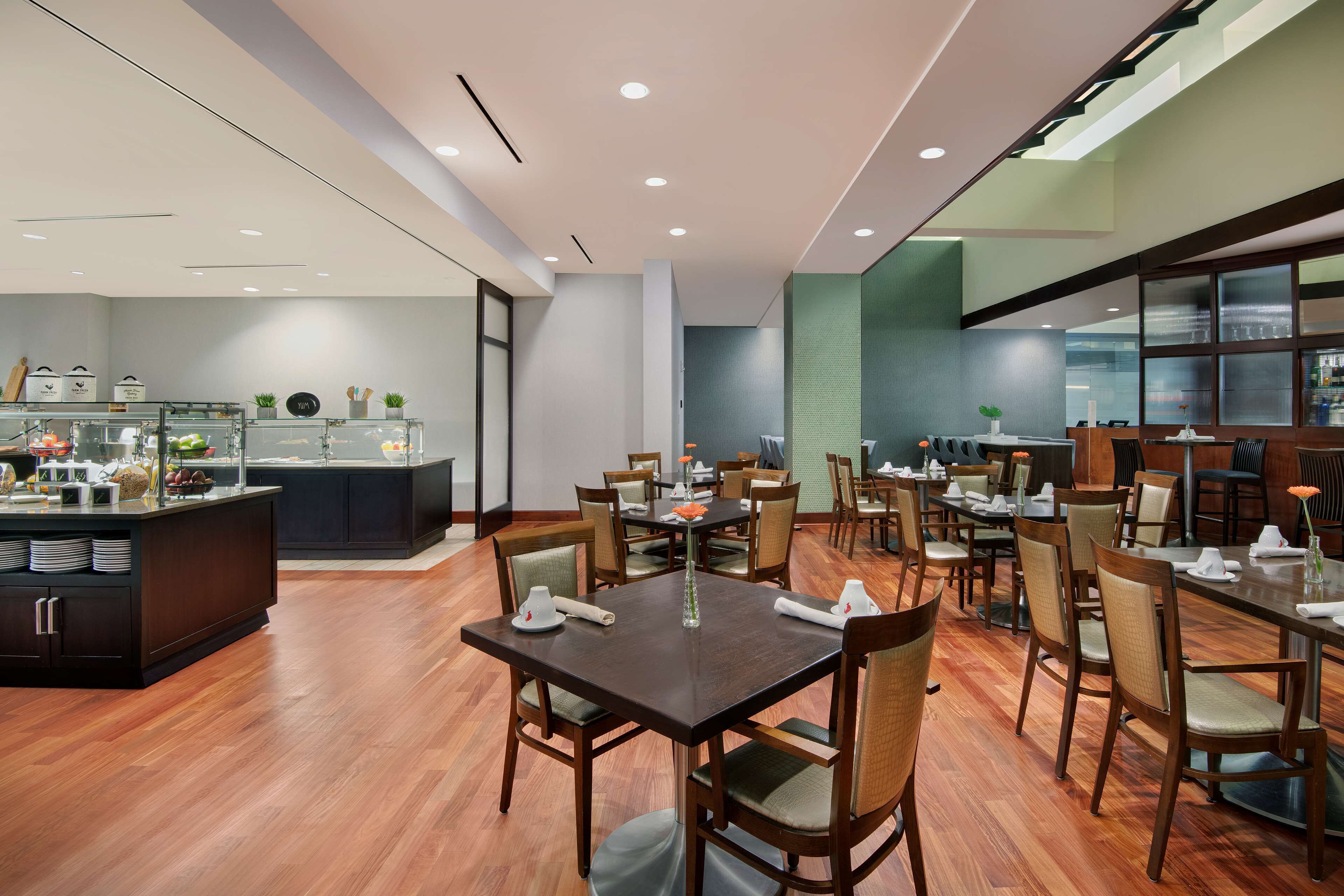 A modern dining area with wooden tables and chairs, a buffet counter, and a large window providing natural light.