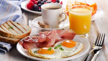 Un plato de desayuno con huevos, prosciutto, tostadas y una taza de café.