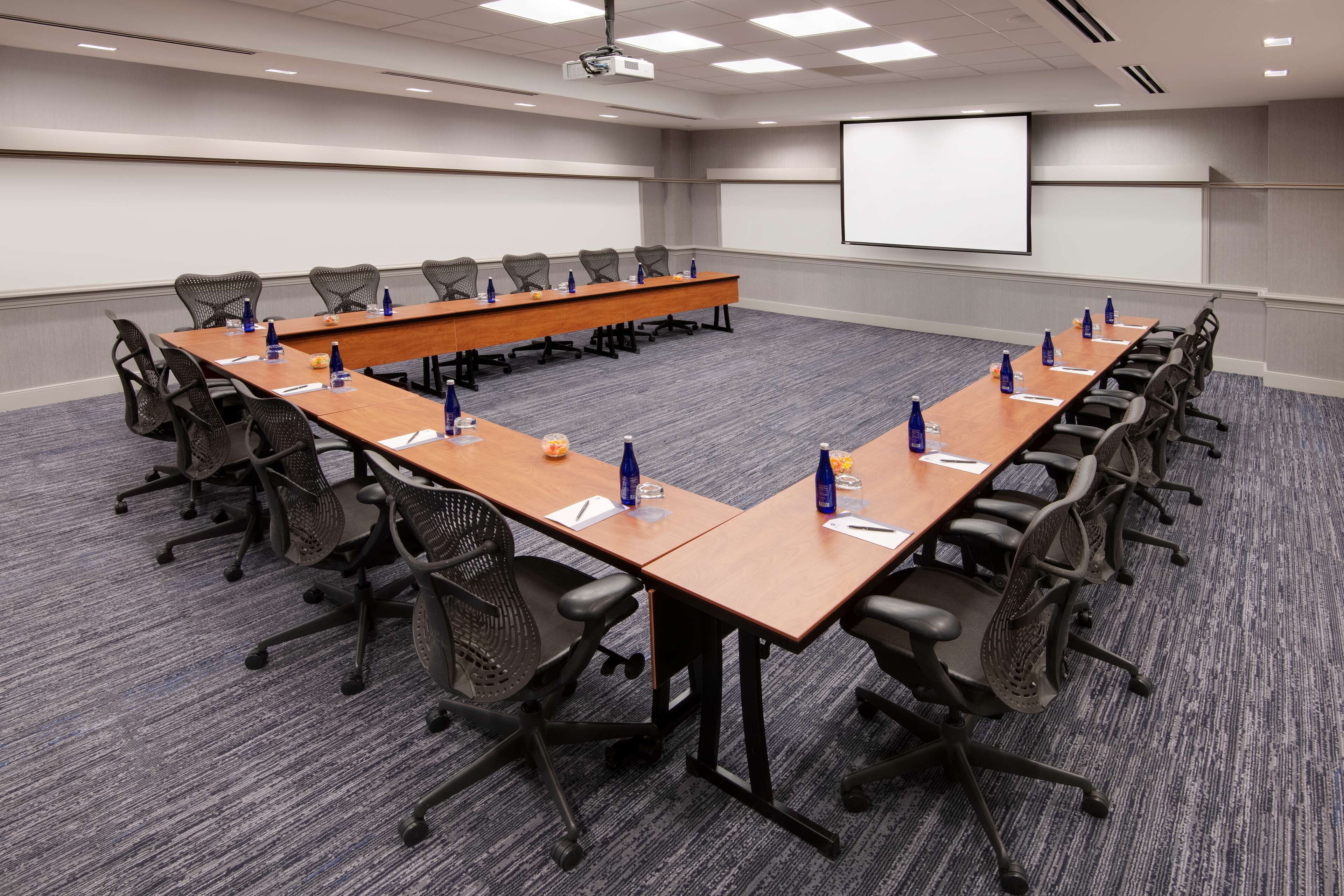 A conference room with a long table, chairs, and a projector screen.