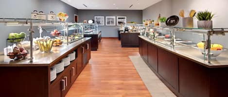 A modern breakfast bar with glass display cases filled with fruits and breakfast items, wooden cabinets, and a clean, tiled floor.