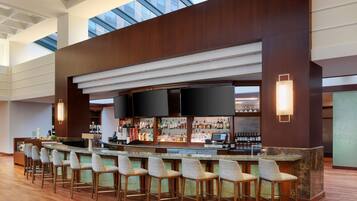 A modern bar area with a long counter, multiple bar stools, and a variety of bottles and glasses.