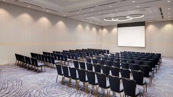 Un salón de conferencias con filas de sillas, una pantalla grande y una alfombra estampada.