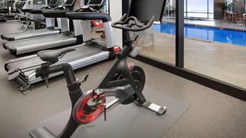Une salle de sport équipée de vélos d’appartement, de tapis de course et d’un espace piscine.