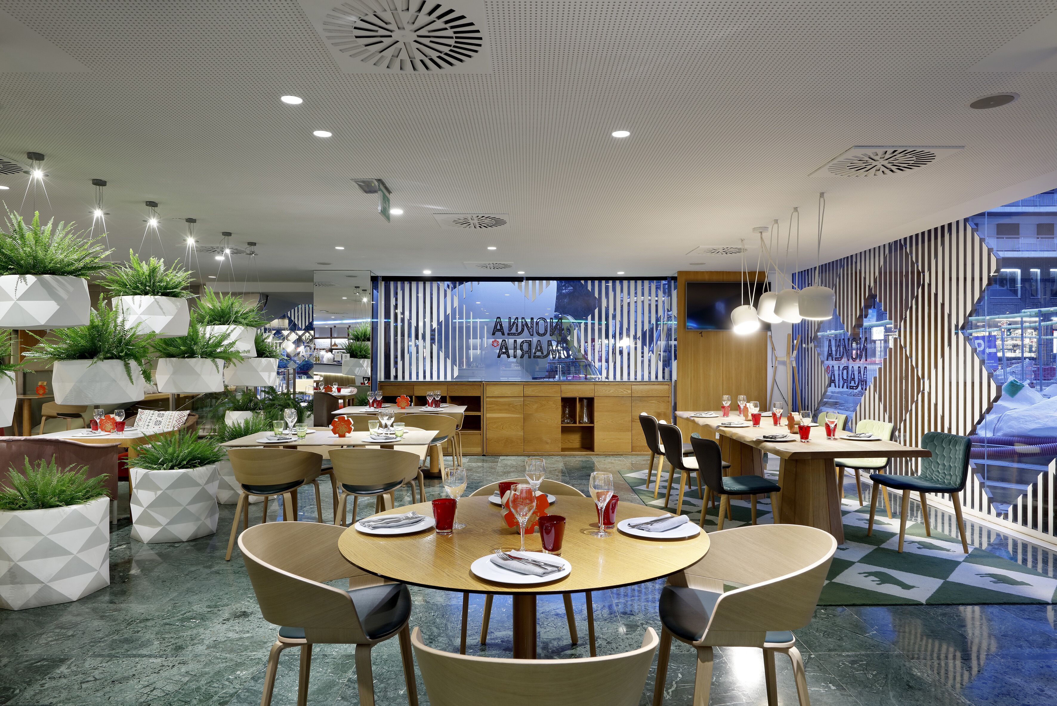 Un restaurante moderno con mesas redondas, sillas y plantas en macetas.