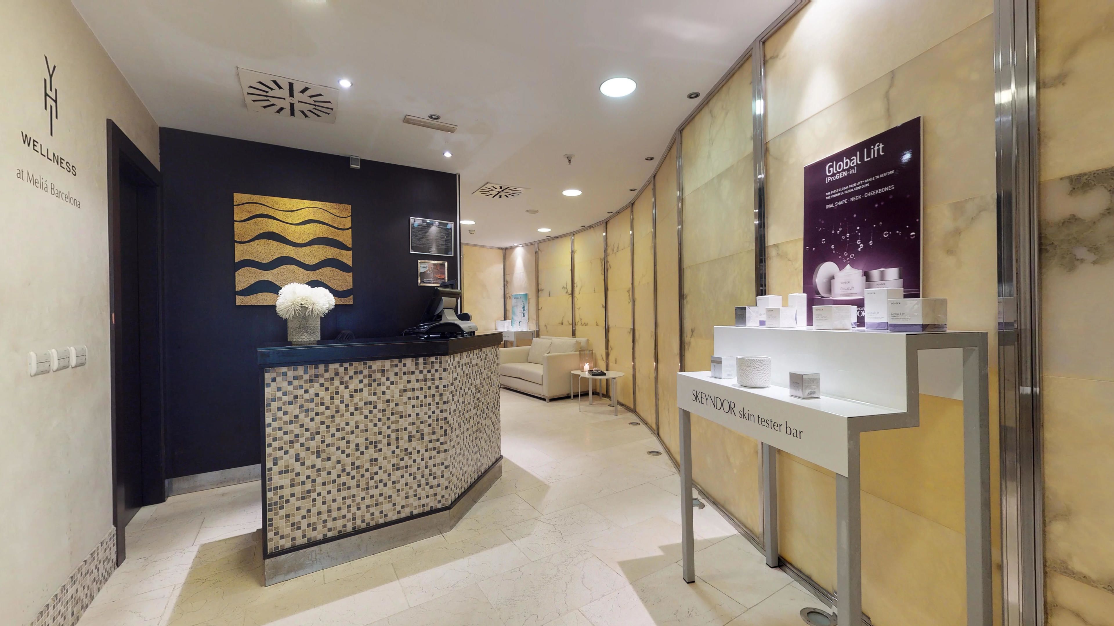 A reception area with a counter, a sofa, a small table with a candle, and a display of skincare products.