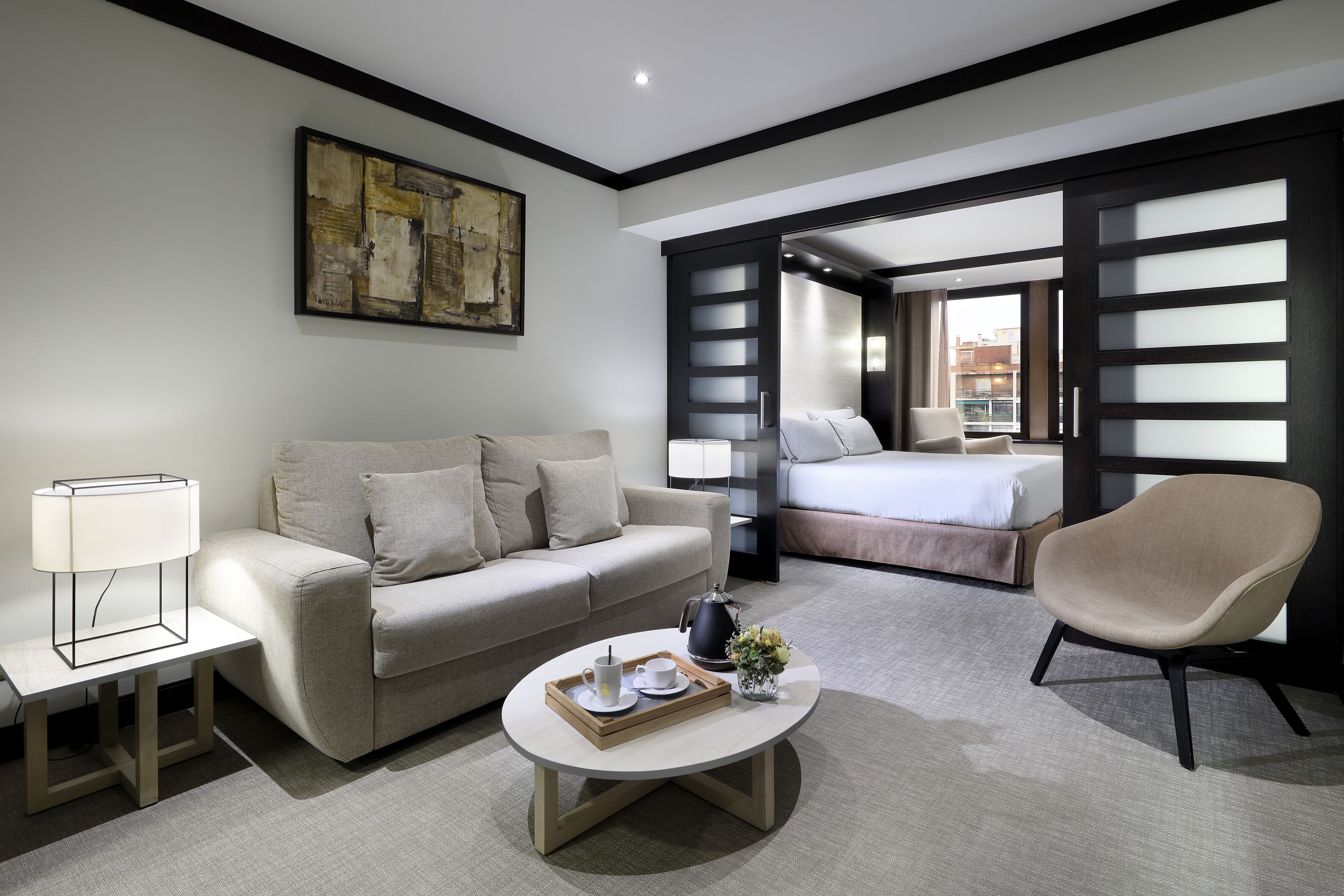A modern hotel room with a sofa, a chair, a coffee table, and a bed.