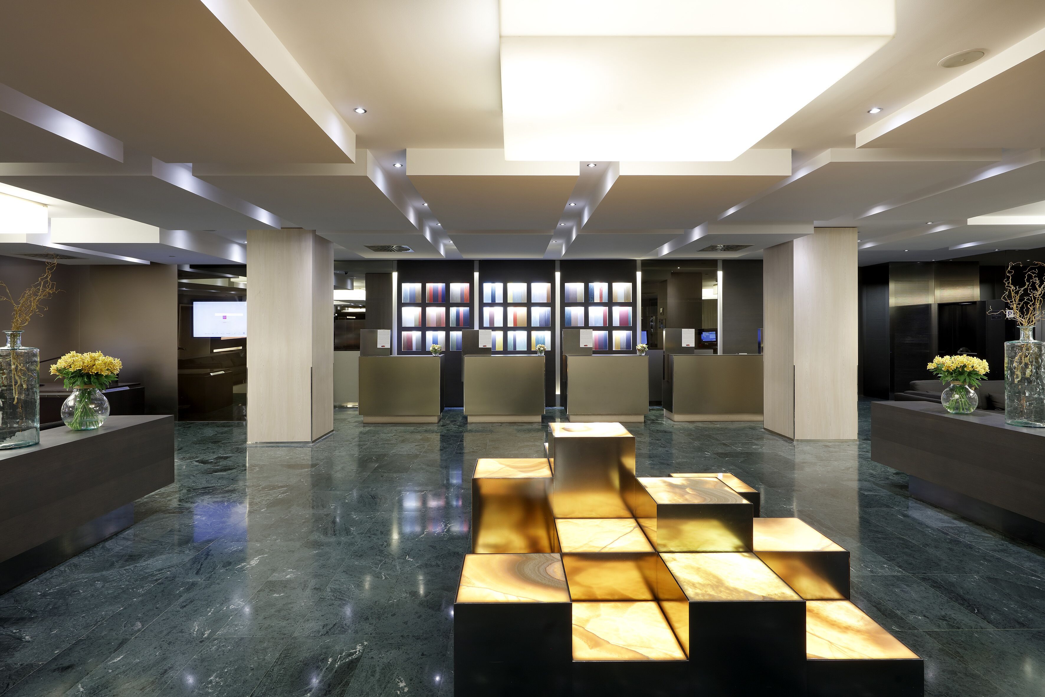 A modern lobby with a central seating area, a reception desk, and a wall of digital displays.