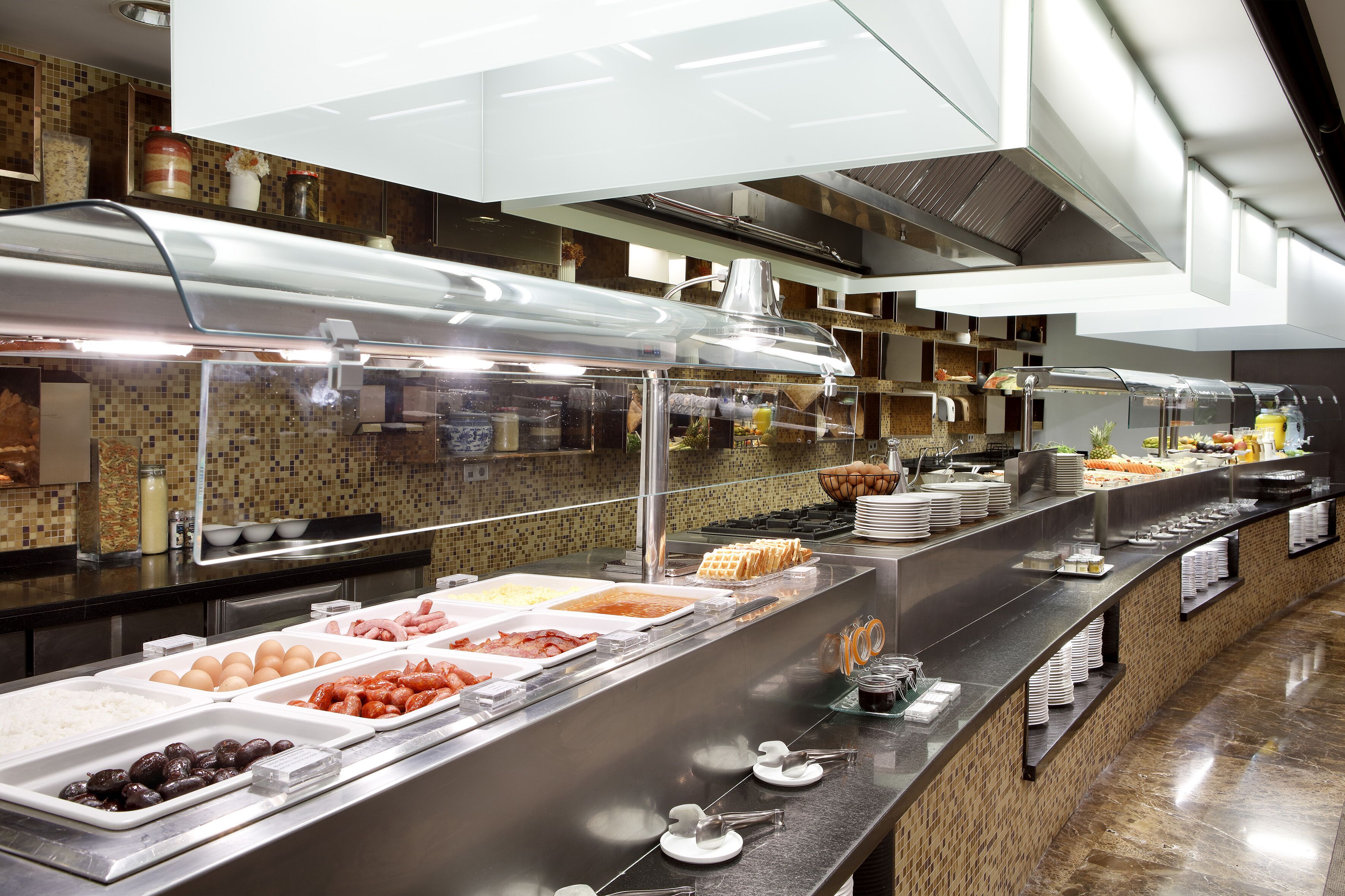 Un bufé con diferentes opciones de comida y una cocina moderna al fondo.