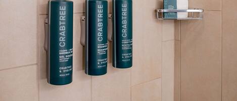 Three bottles of Crabtree & Evelyn shampoo and conditioner on a wall-mounted shelf in a bathroom.