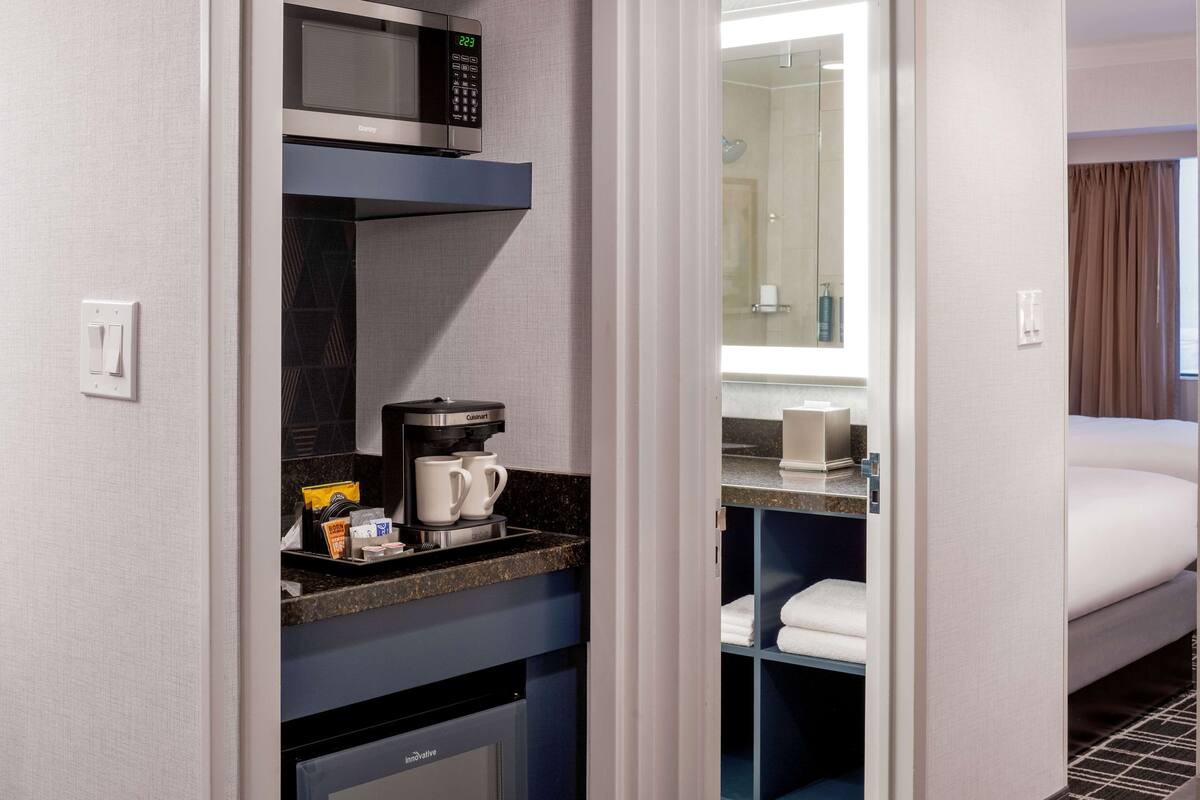 A compact hotel room with a kitchenette, including a microwave, coffee maker, and mini-fridge.