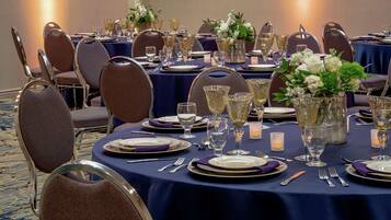 A banquet table set with fine china, silverware, and crystal glassware, surrounded by upholstered chairs.