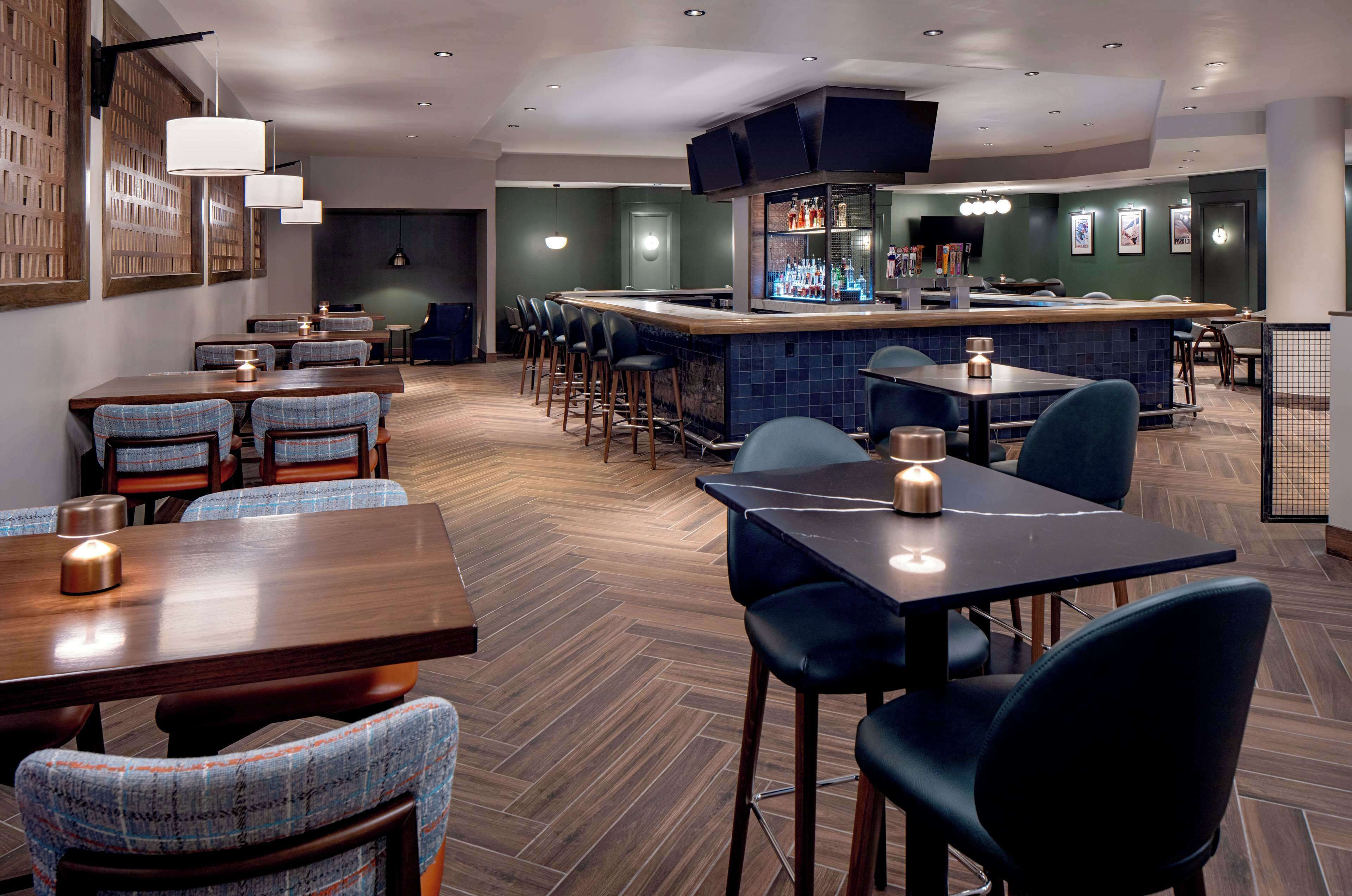 A modern restaurant with a bar area, wooden flooring, and a mix of bar and booth seating.