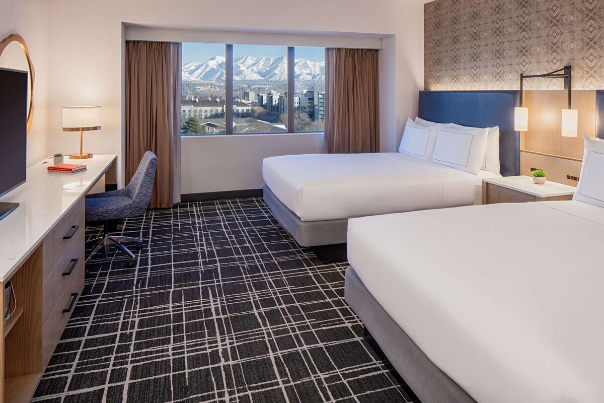 Habitación de hotel con cama, escritorio, una silla y vistas a montañas.