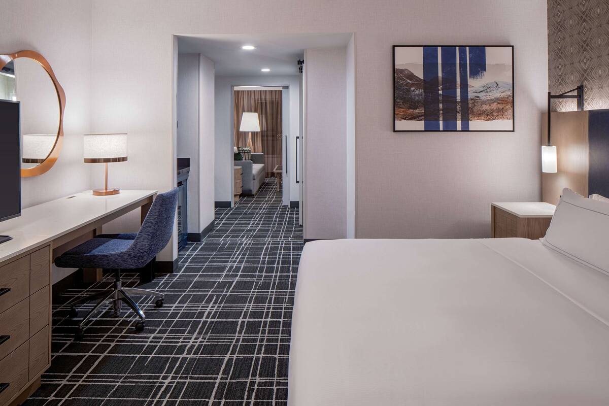 A hotel room with a bed, desk, chair, and a painting on the wall.