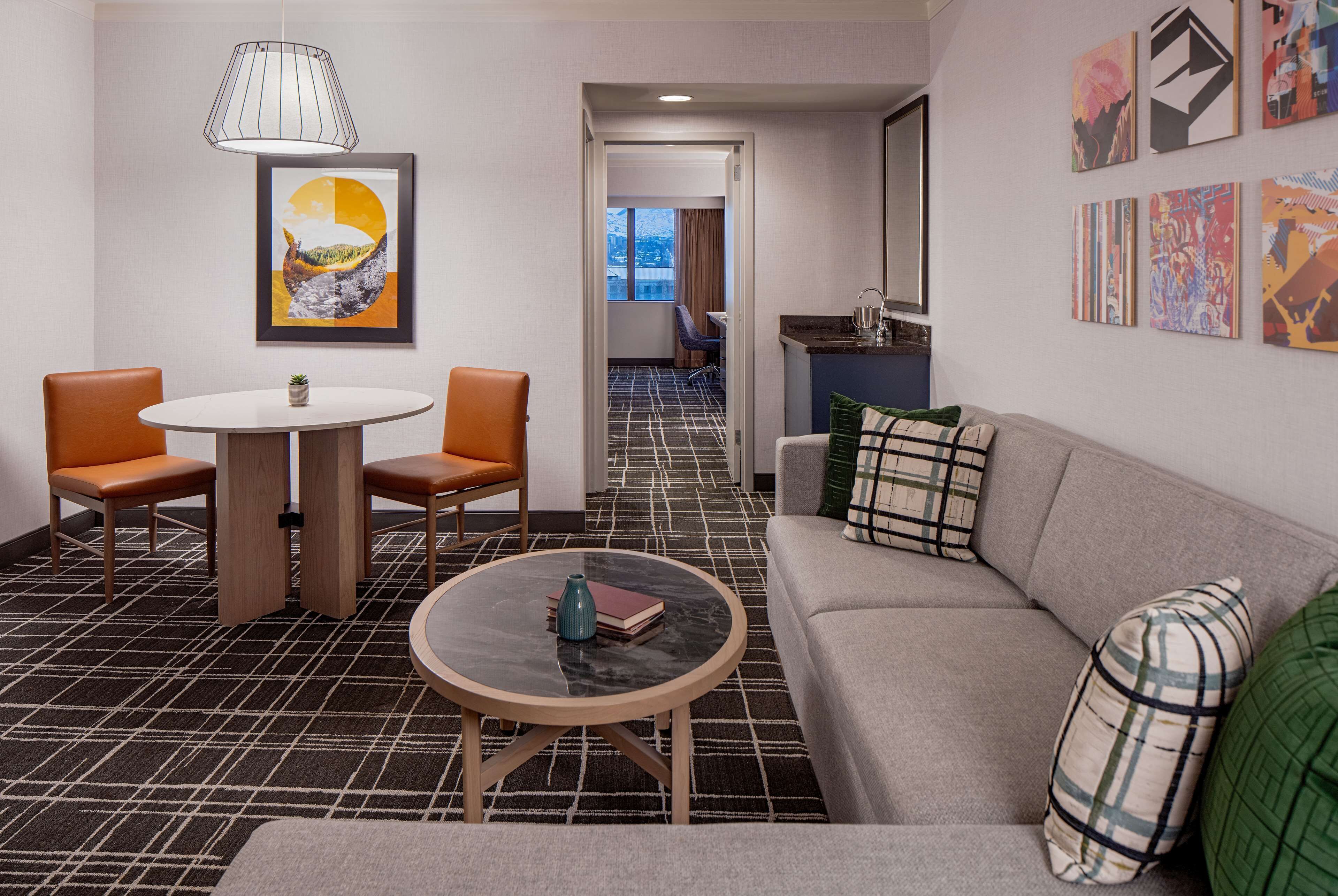 Habitación de hotel con comedor, sofá, mesa redonda y obras de arte en las paredes.