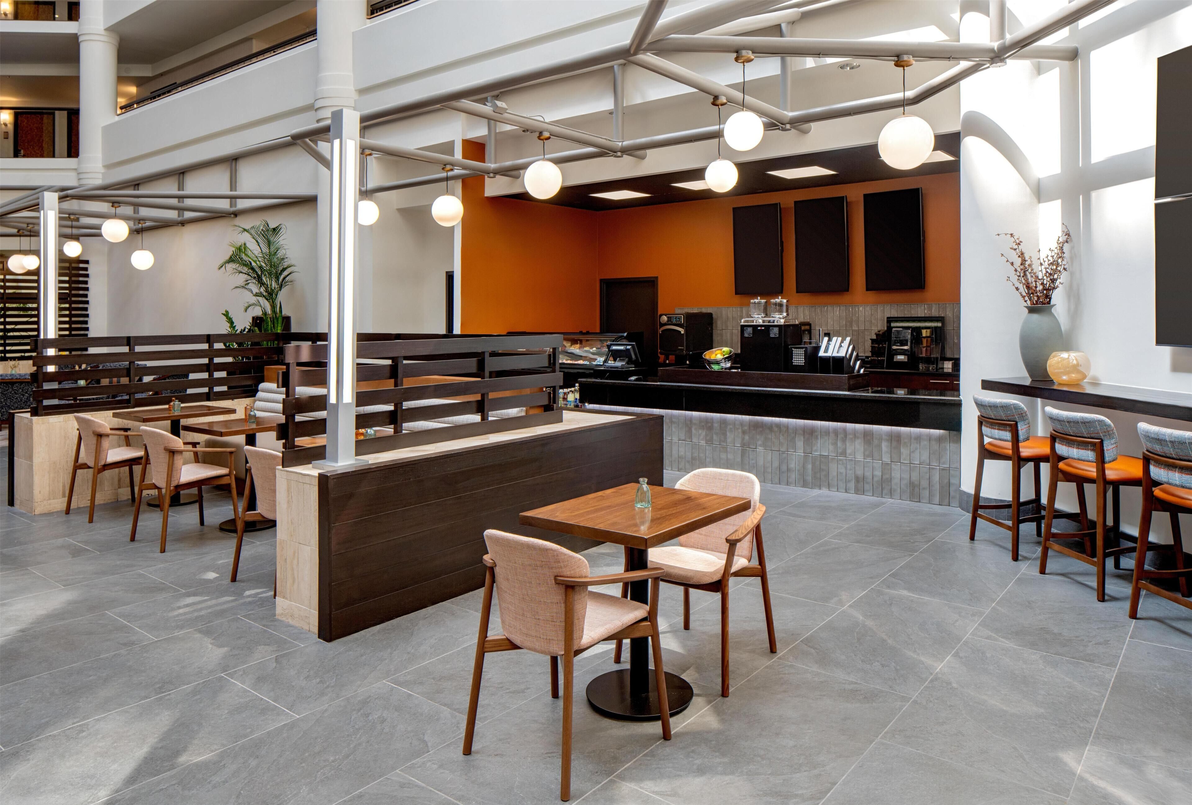 En modern restaurang med höga bord och stolar, en bardisk med en kaffemaskin och en sittgrupp med utsikt över interiören.