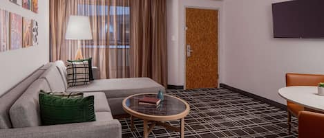 A hotel room with a sofa, a round table, a TV, and a door.