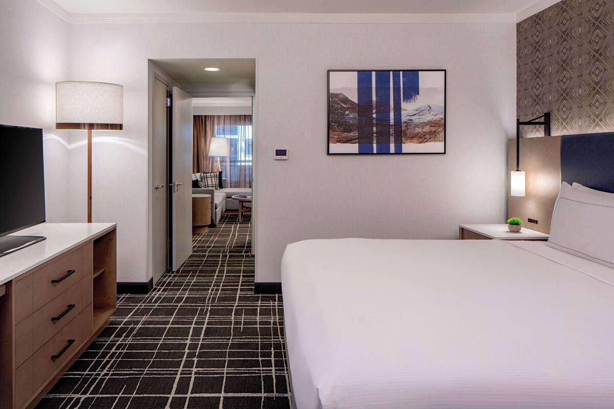 A hotel room with a large bed, a desk with a lamp, a TV, and a painting on the wall.