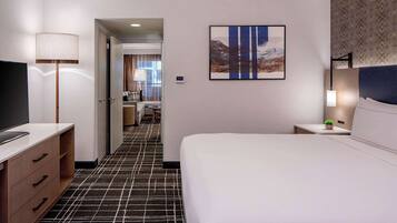 A hotel room with a large bed, a desk with a lamp, a TV, and a painting on the wall.