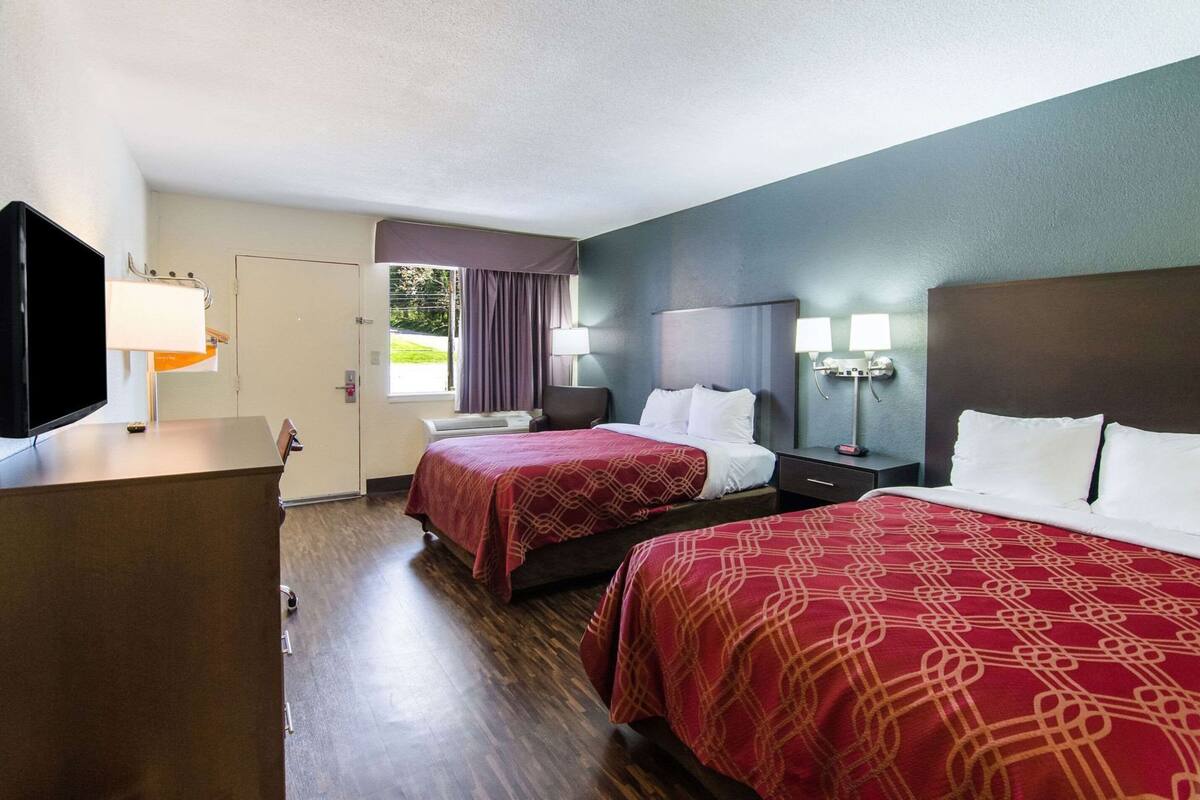 Habitación de hotel con dos camas, televisor, escritorio y ventana con cortinas.