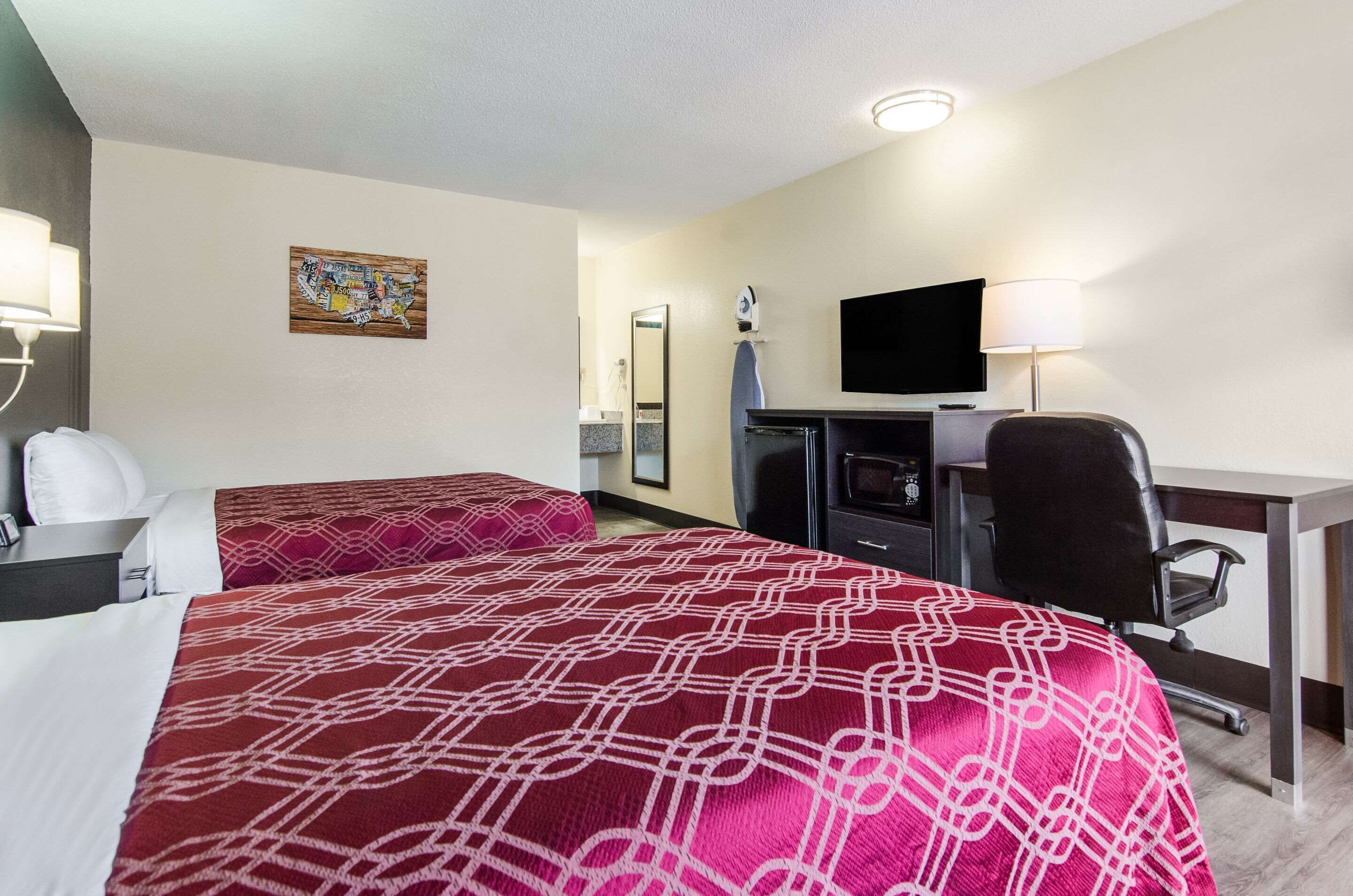 Habitación de hotel con dos camas, un escritorio, una silla, un televisor y un espejo de baño.