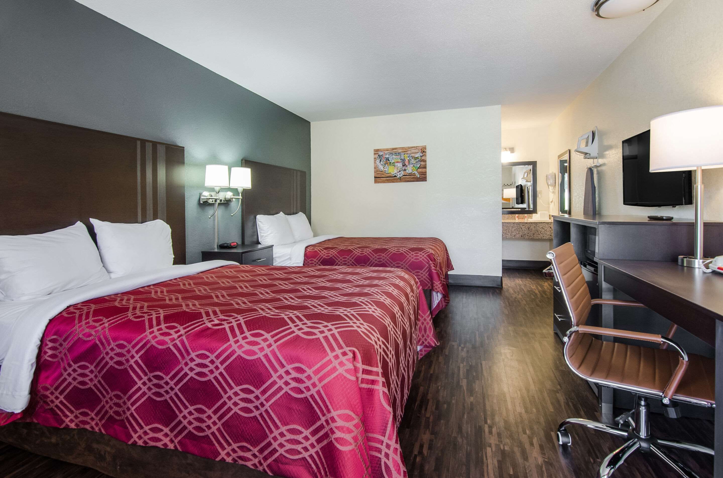 A hotel room with two beds, a desk, a chair, a TV, and a bathroom mirror.