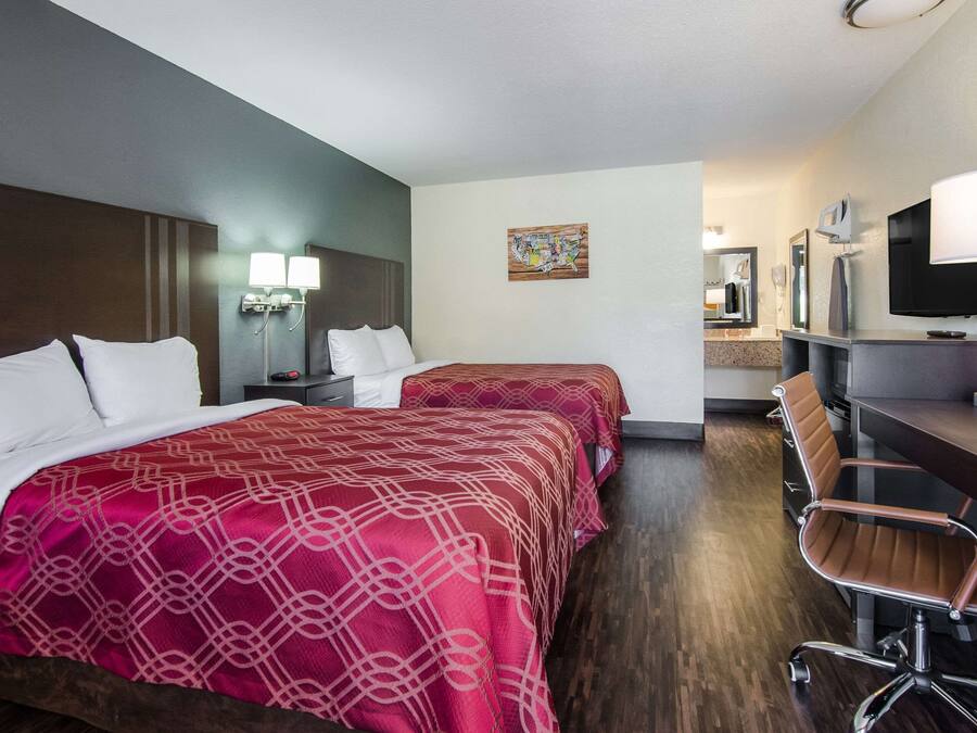 A hotel room with two beds, a desk, a chair, a TV, and a bathroom mirror.