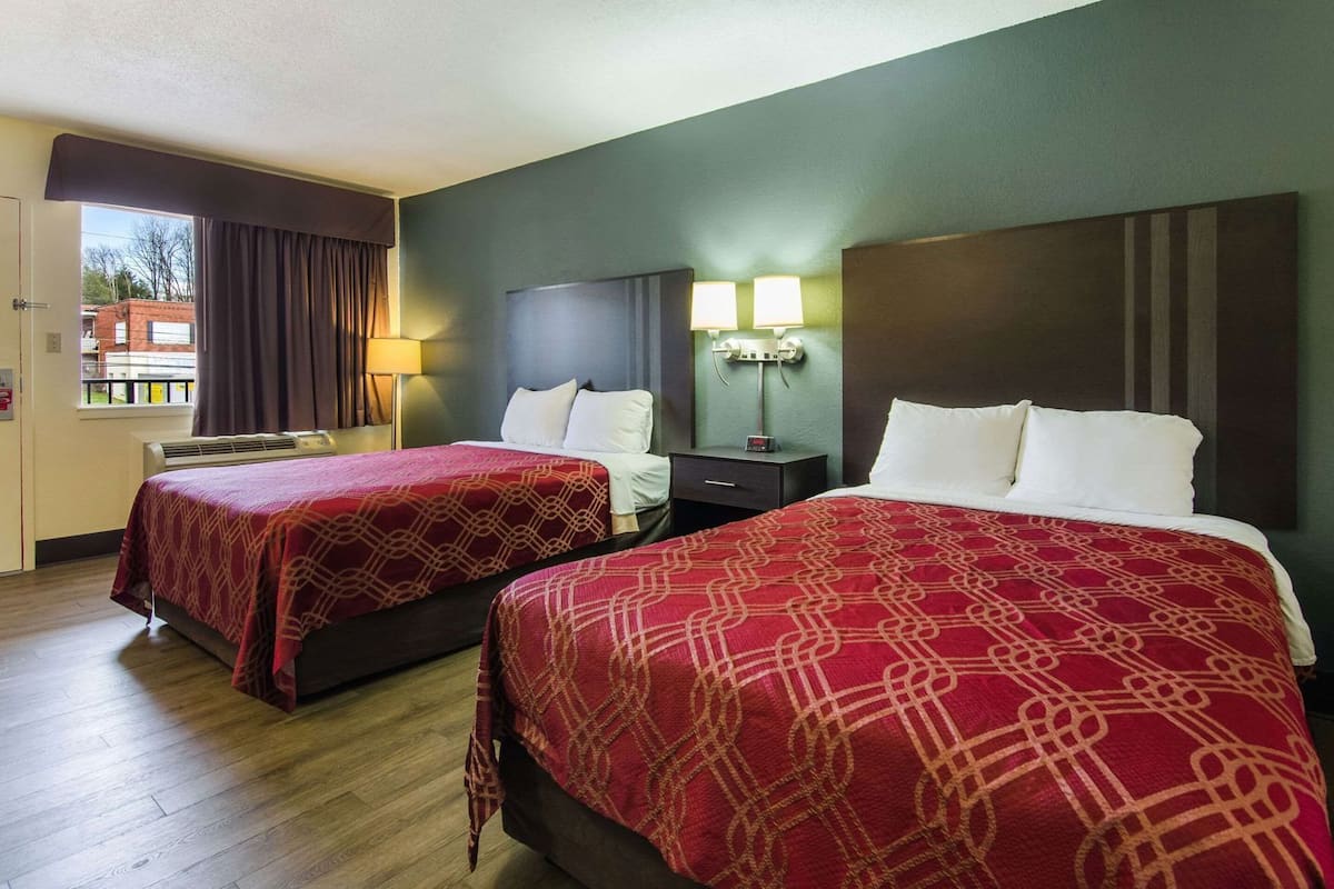 Habitación de hotel con dos camas, una mesita de noche, una lámpara y una ventana con cortinas.