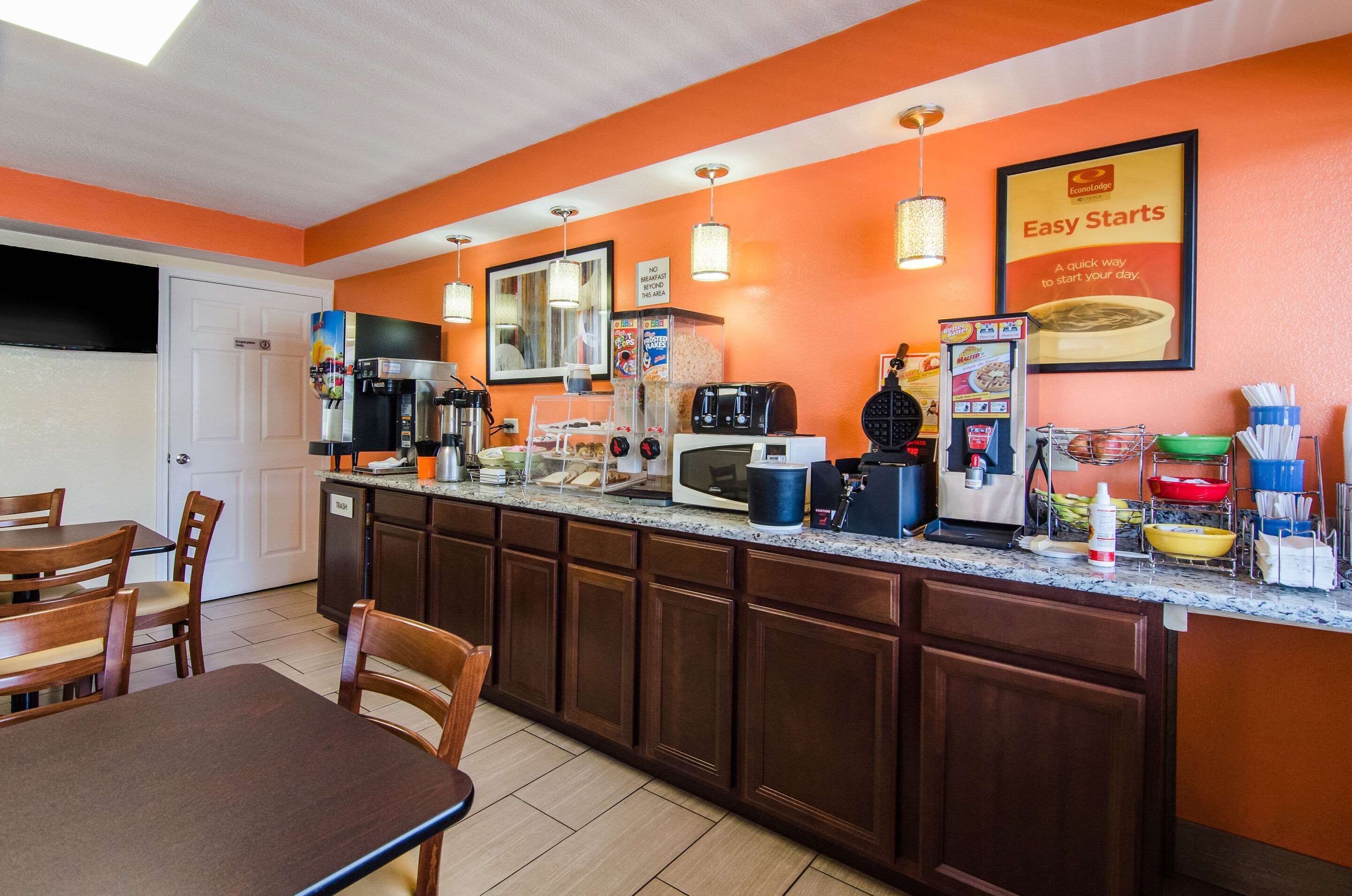 A compact kitchen with a coffee machine, microwave, and toaster. There are wooden cabinets and a small dining area with chairs.