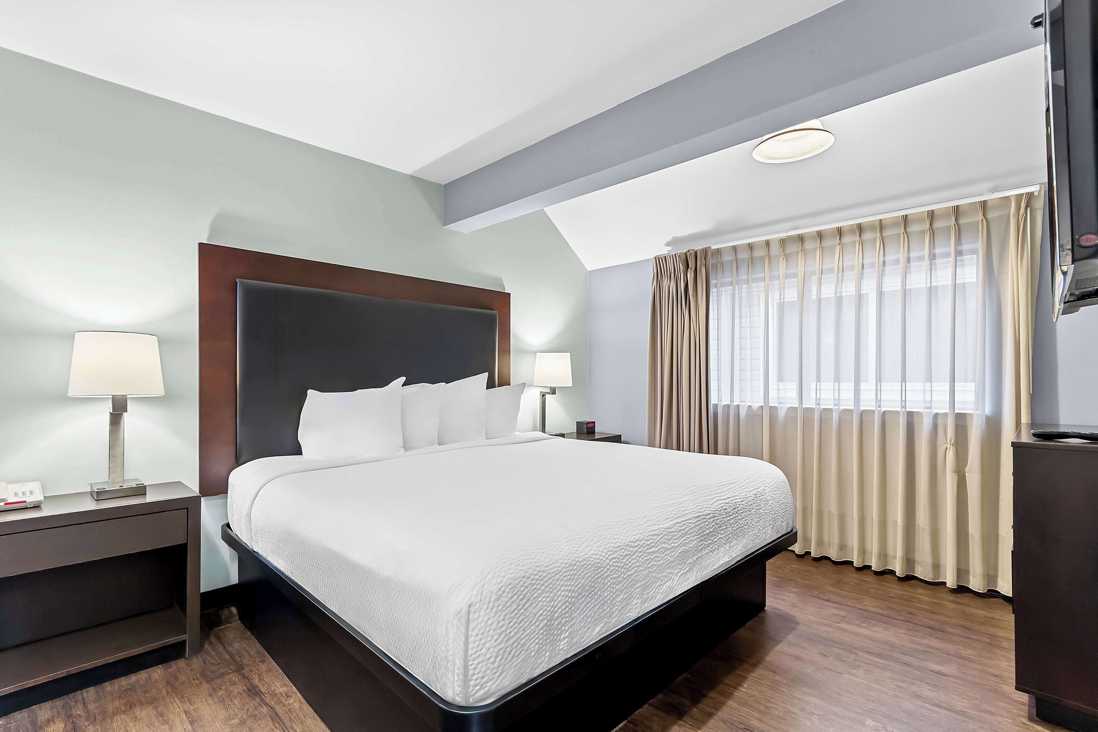 Una habitación de hotel con una cama grande, dos mesitas de noche con lámparas, un televisor y una ventana con cortinas.