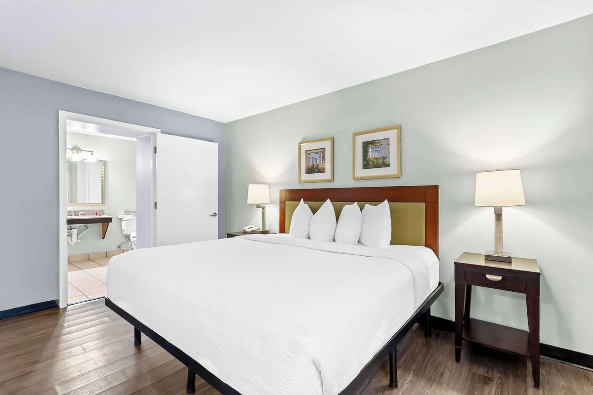 A hotel room with a large bed, bedside lamps, a nightstand, and a door leading to a bathroom.