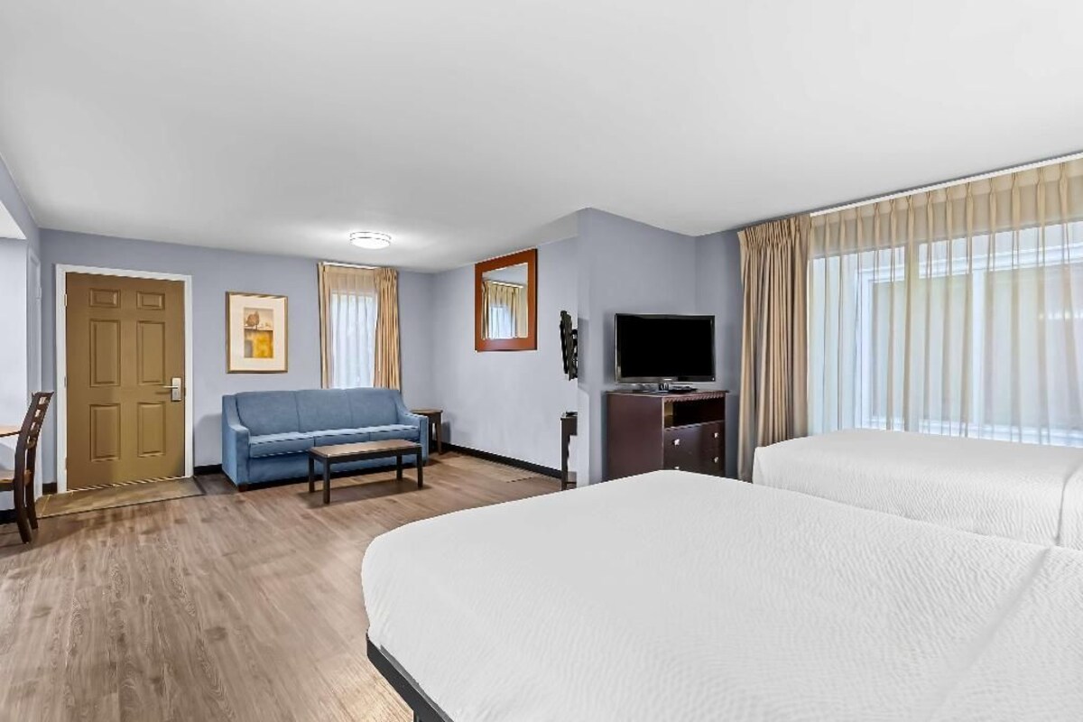 A hotel room with a large bed, a sofa, a TV, and a wooden floor.