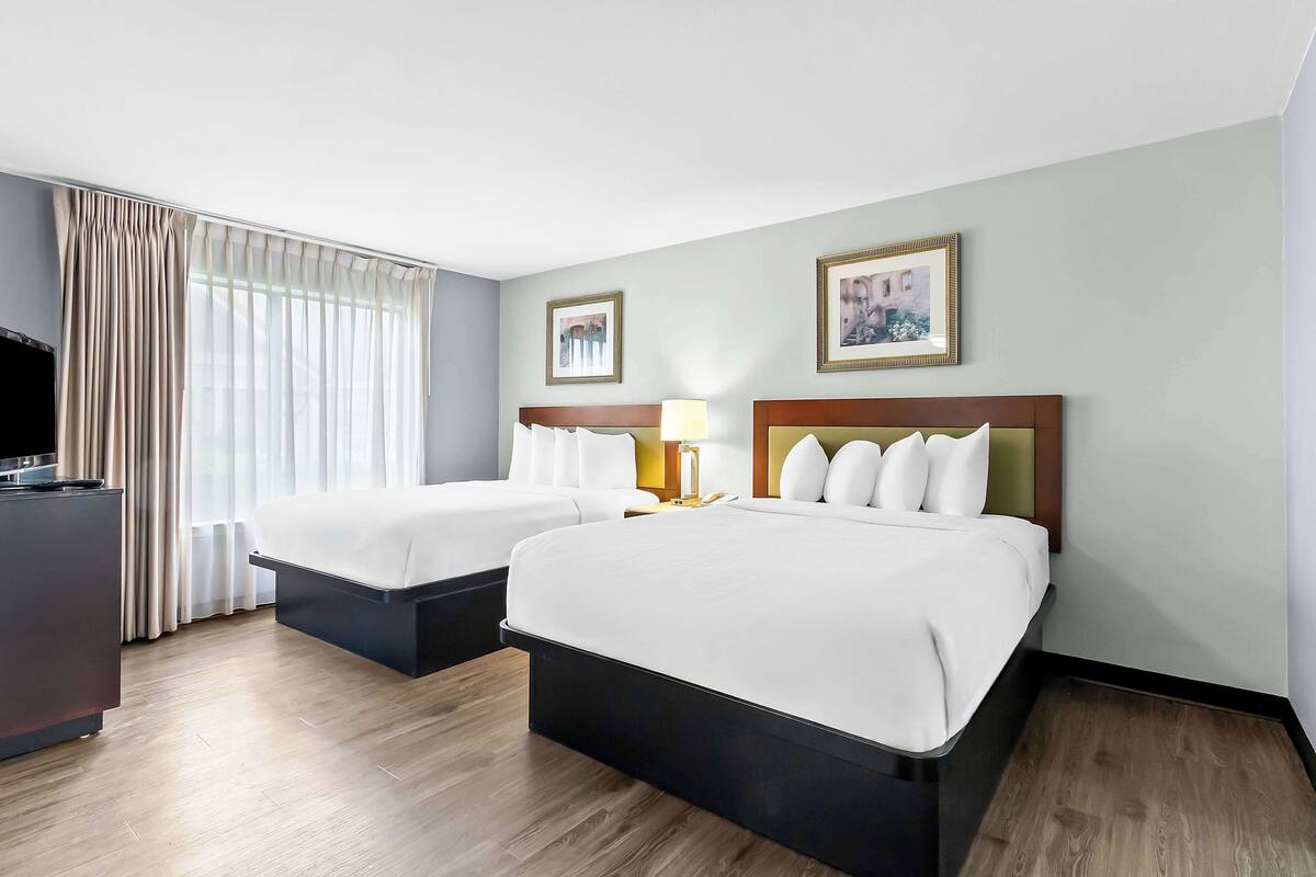 A hotel room with two beds, a desk, and a TV.