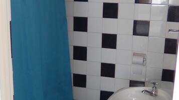 Un bany petit amb un lavabo blanc, una cortina de bany blava i un tapet de terra amb dibuixos.