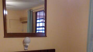 A single bed with a wooden headboard, a bedside lamp, and a mirror above it.
