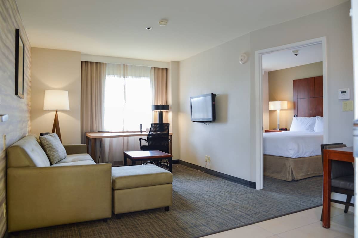 A hotel room with a sofa, a small table, a TV, and a bed.