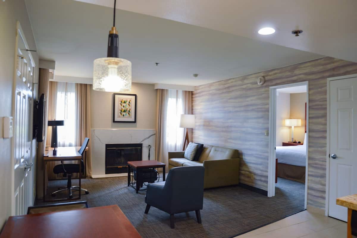 A hotel room with a fireplace, a sofa, a dining area with a table and chairs, and a bed.