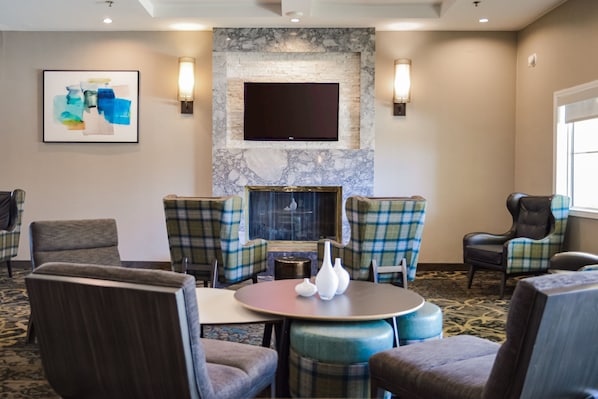 A hotel room with a fireplace, plaid chairs, a round table, and a flat-screen TV mounted on the wall. - Residence Inn by Marriott La Mirada Buena Park (La Mirada)